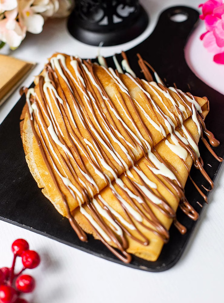 side view of crepe with chocolate cocoa syrup on a wooden cutting board